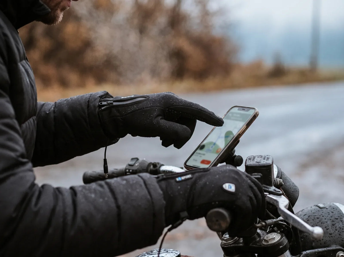 Alpenwarm HeatGlove Pro heated gloves on a motorcycle handlebar, operating a touchscreen