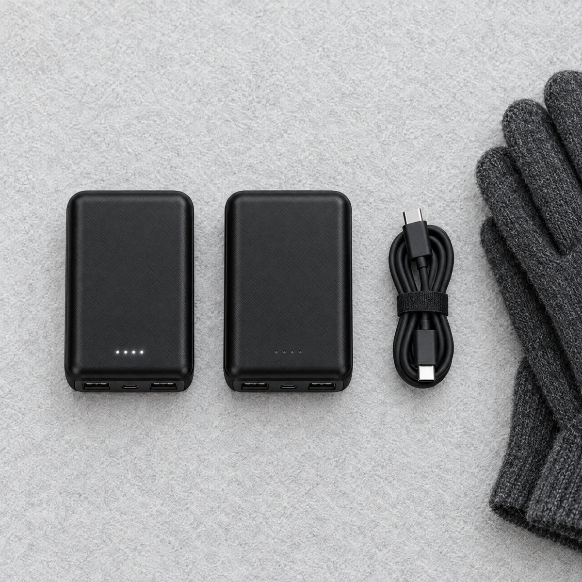 Zwei Powerbanks nebeneinander mit USB-C-Kabel und Handschuhen, eine davon voll geladen